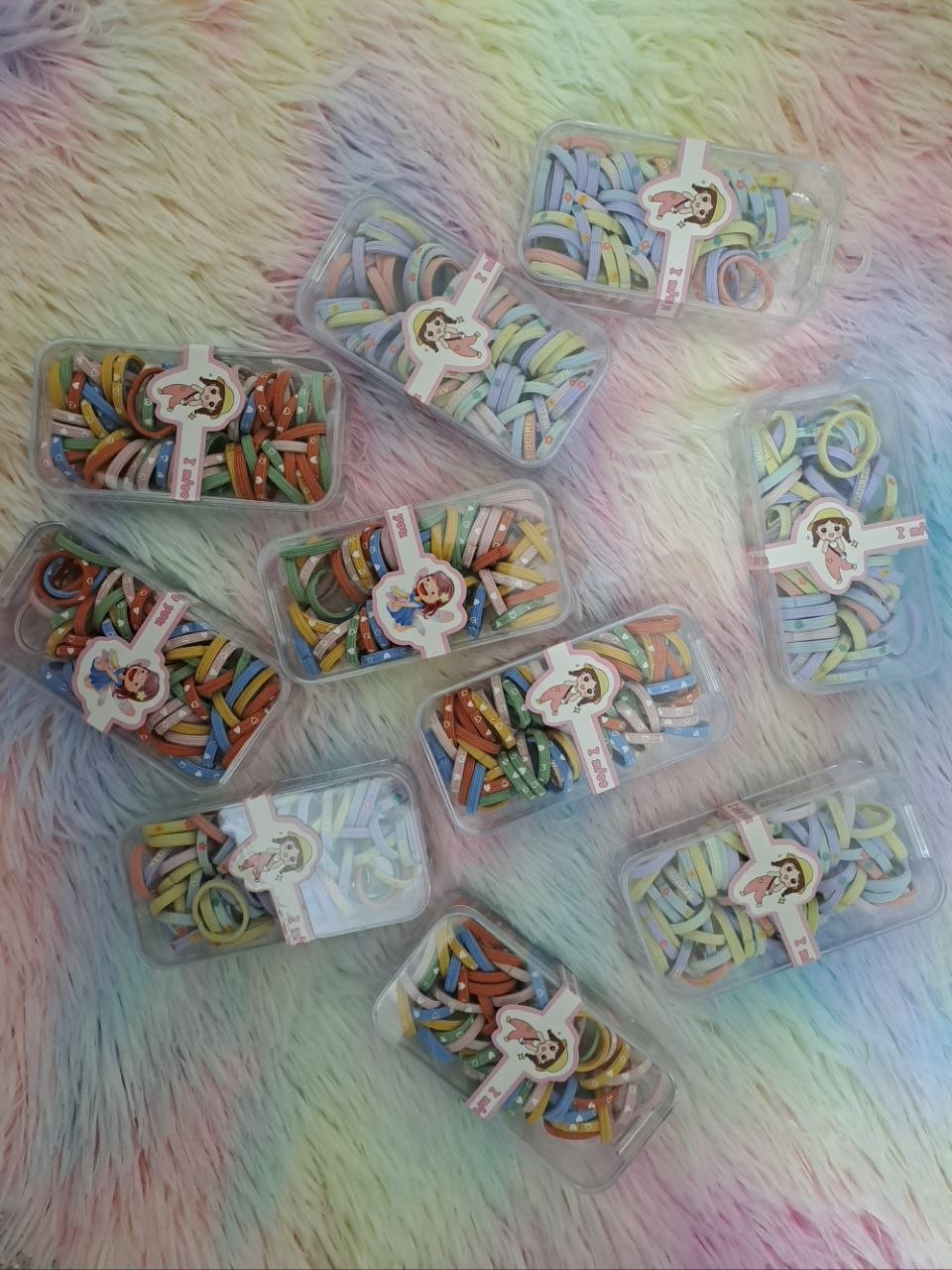 Clear storage containers filled with colorful rainbow thin elastic hair ties in various solid and multicolor combinations for girls