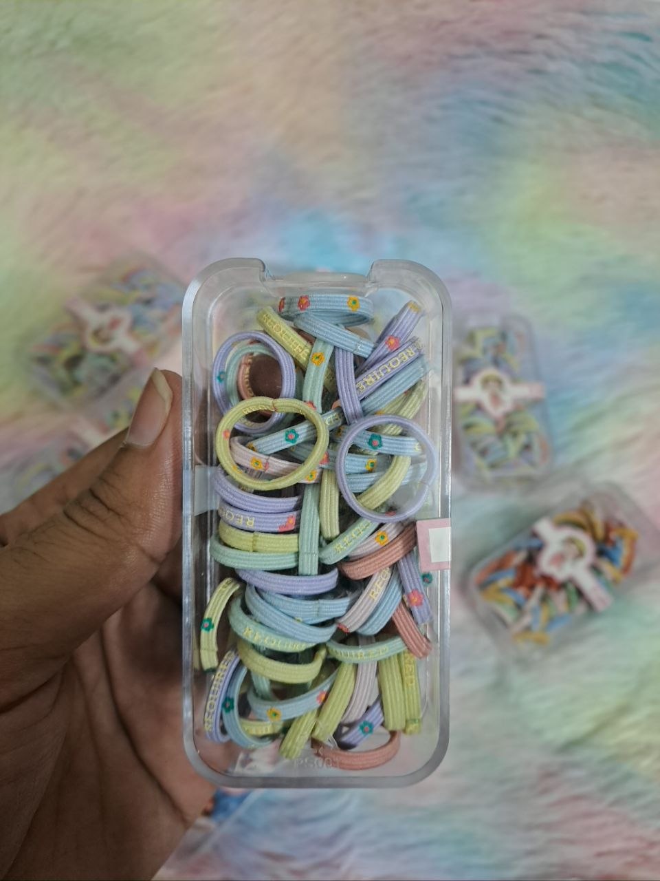 Clear storage containers filled with colorful rainbow thin elastic hair ties in various solid and multicolor combinations for girls