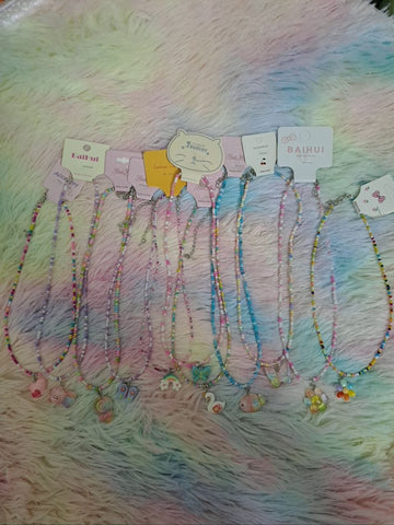 Colorful beaded necklaces with tiny rainbow beads and adorable charm pendants including smiling faces, flowers, hearts, and rainbows for girls