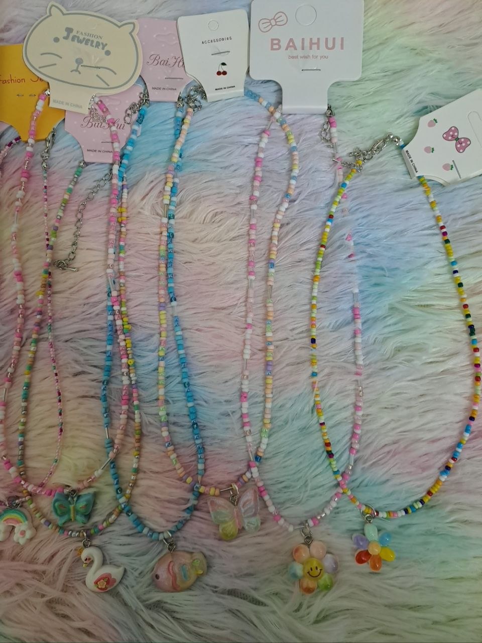 Colorful beaded necklaces with tiny rainbow beads and adorable charm pendants including smiling faces, flowers, hearts, and rainbows for girls