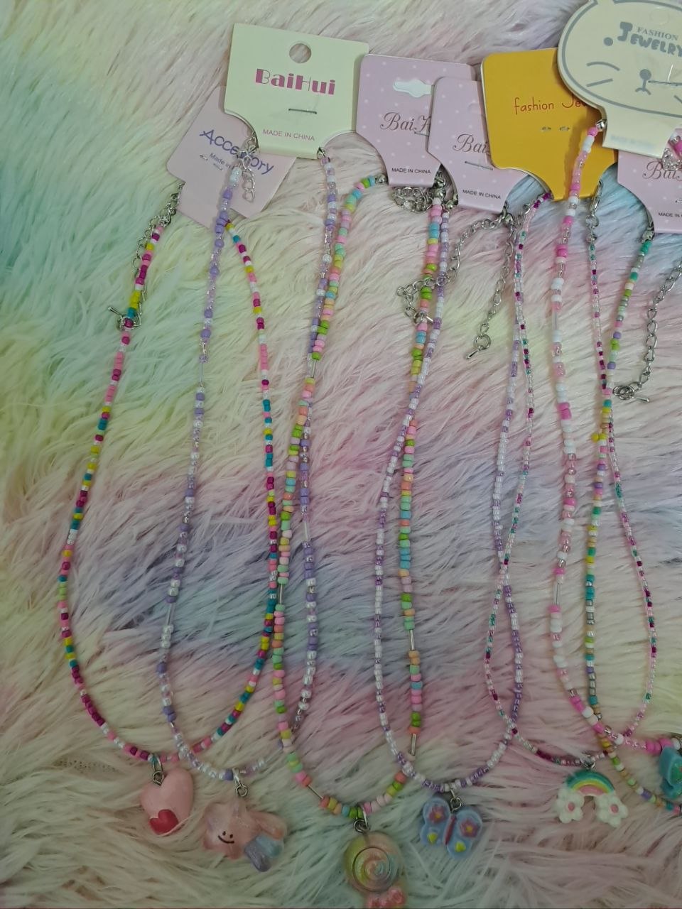 Colorful beaded necklaces with tiny rainbow beads and adorable charm pendants including smiling faces, flowers, hearts, and rainbows for girls