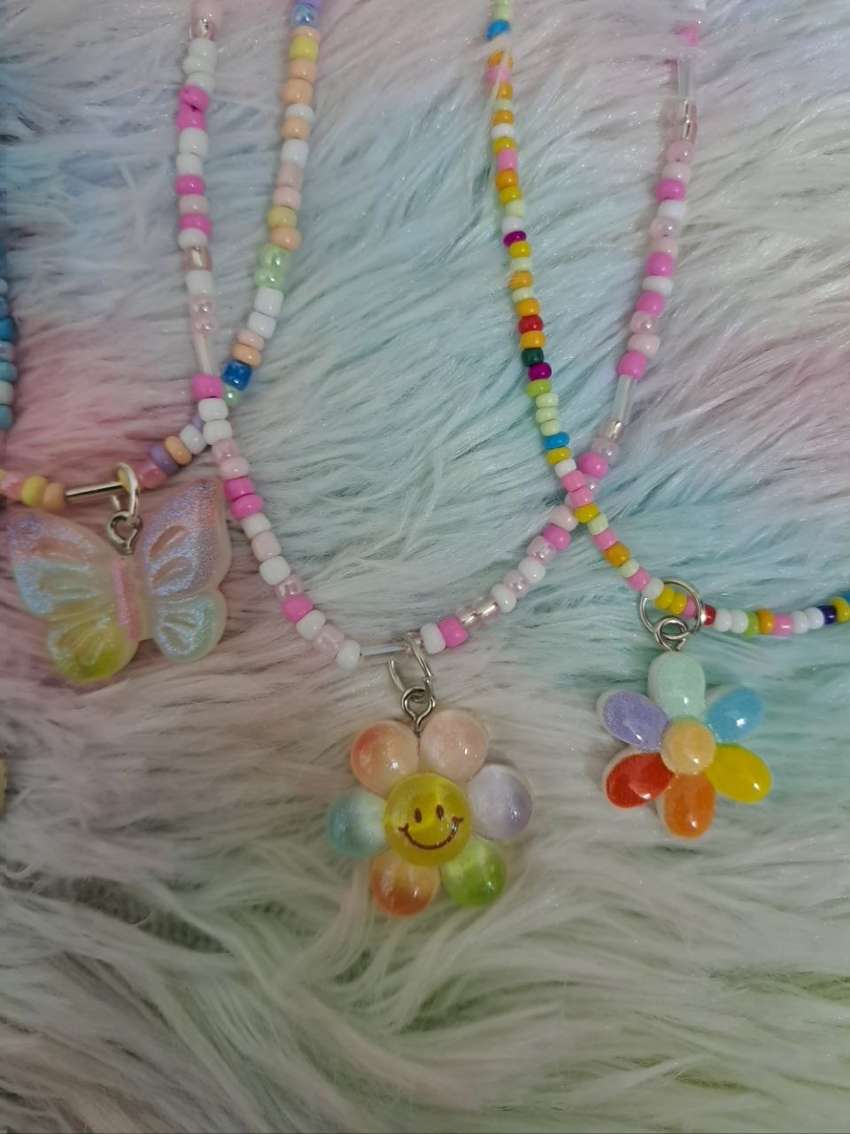 Colorful beaded necklaces with tiny rainbow beads and adorable charm pendants including smiling faces, flowers, hearts, and rainbows for girls