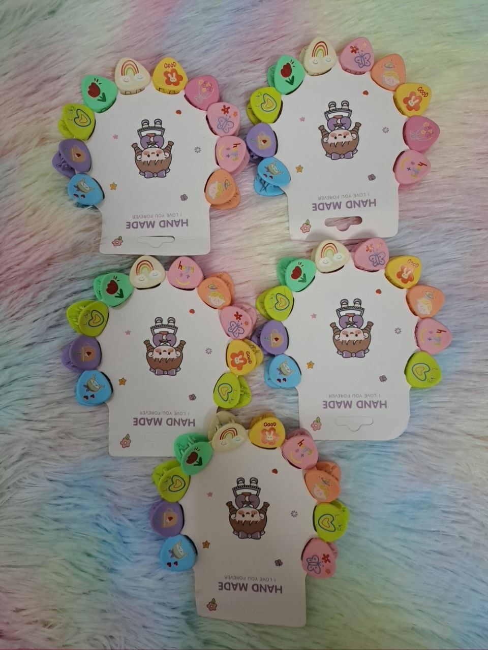Colorful heart-shaped elastic hair ties with cute graphics including rainbows, strawberries, and flowers on Hand Made branded cards for girls