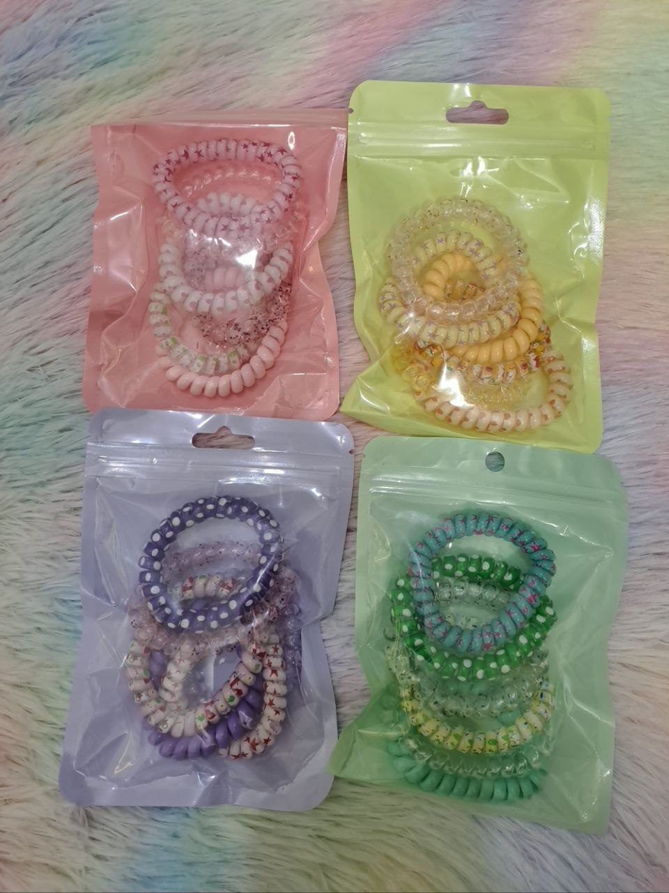 Spiral coil telephone-cord-style hair ties in pastel colors including pink, yellow, purple, and green packaged in color-coordinated sets for girls