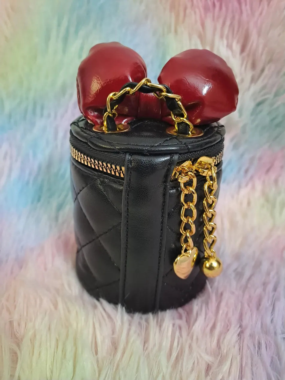 Black quilted faux leather cylinder bag with red boxing glove closure detail and gold chain strap for girls
