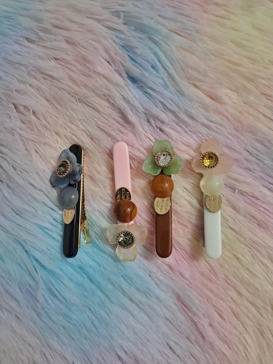 
Floral rhinestone enamel hair clip barrette set in four colourways: black with blue flower, blush pink, deep brown with green blossom, and ivory white with pink bloom, each featuring crystal rhinestone centre, elegant hair accessory