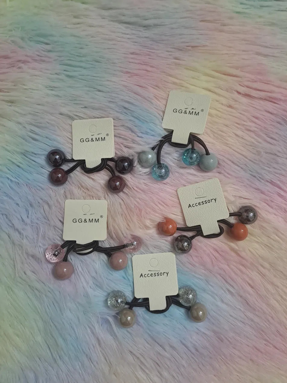 GG&MM beaded ball ponytail hair elastic set in four colour packs: burgundy-plum, teal-marble, blush-glitter, and terracotta-silver, with decorative ball charms in matte, pearl, glitter and marble finishes on double dark elastic
