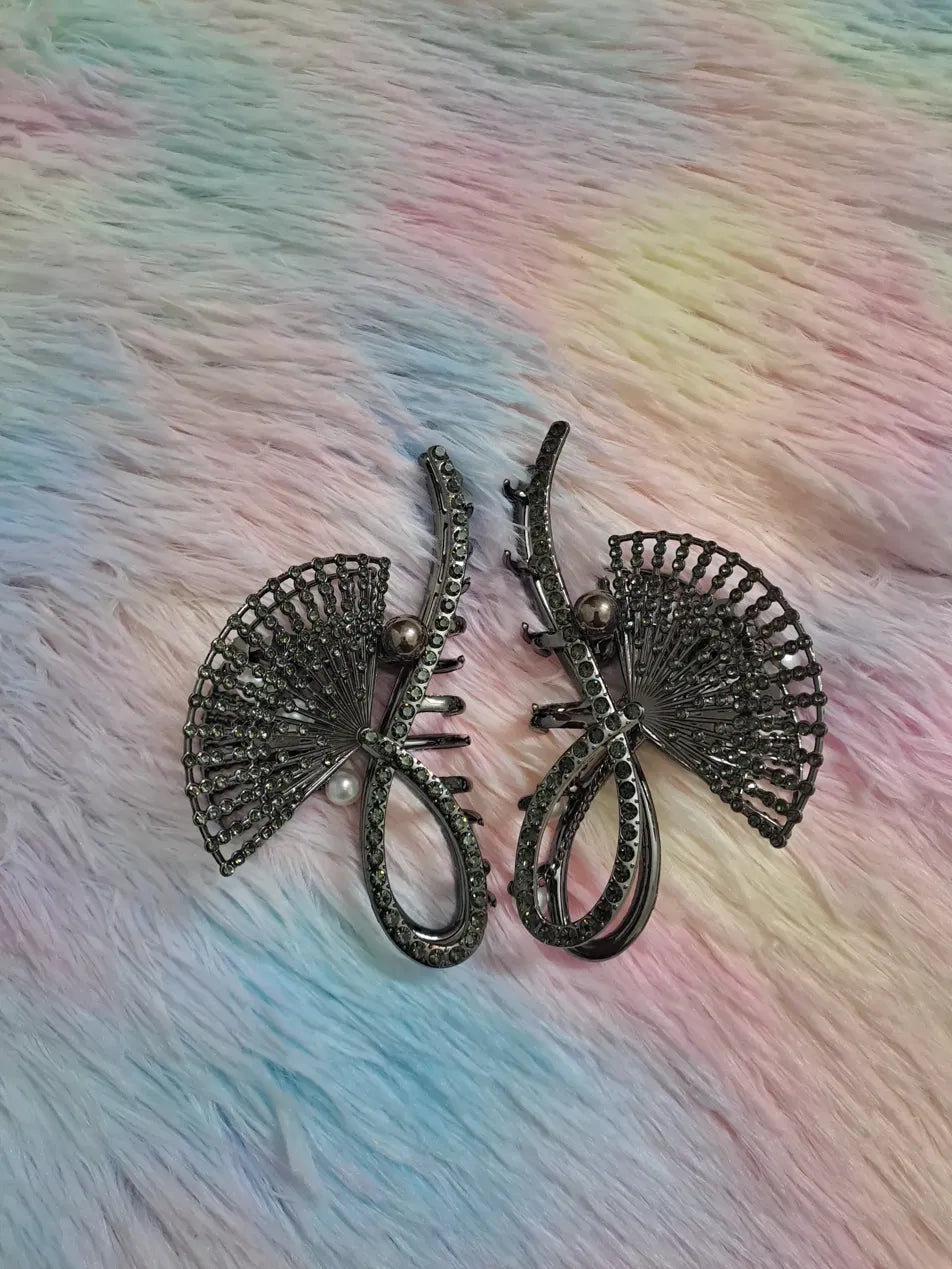 Gunmetal rhinestone fan hair clip pair with radiating spoke structure densely set with dark smoky rhinestones and single pearl accent, art deco architectural design, claw mechanism, dramatic formal hair accessory