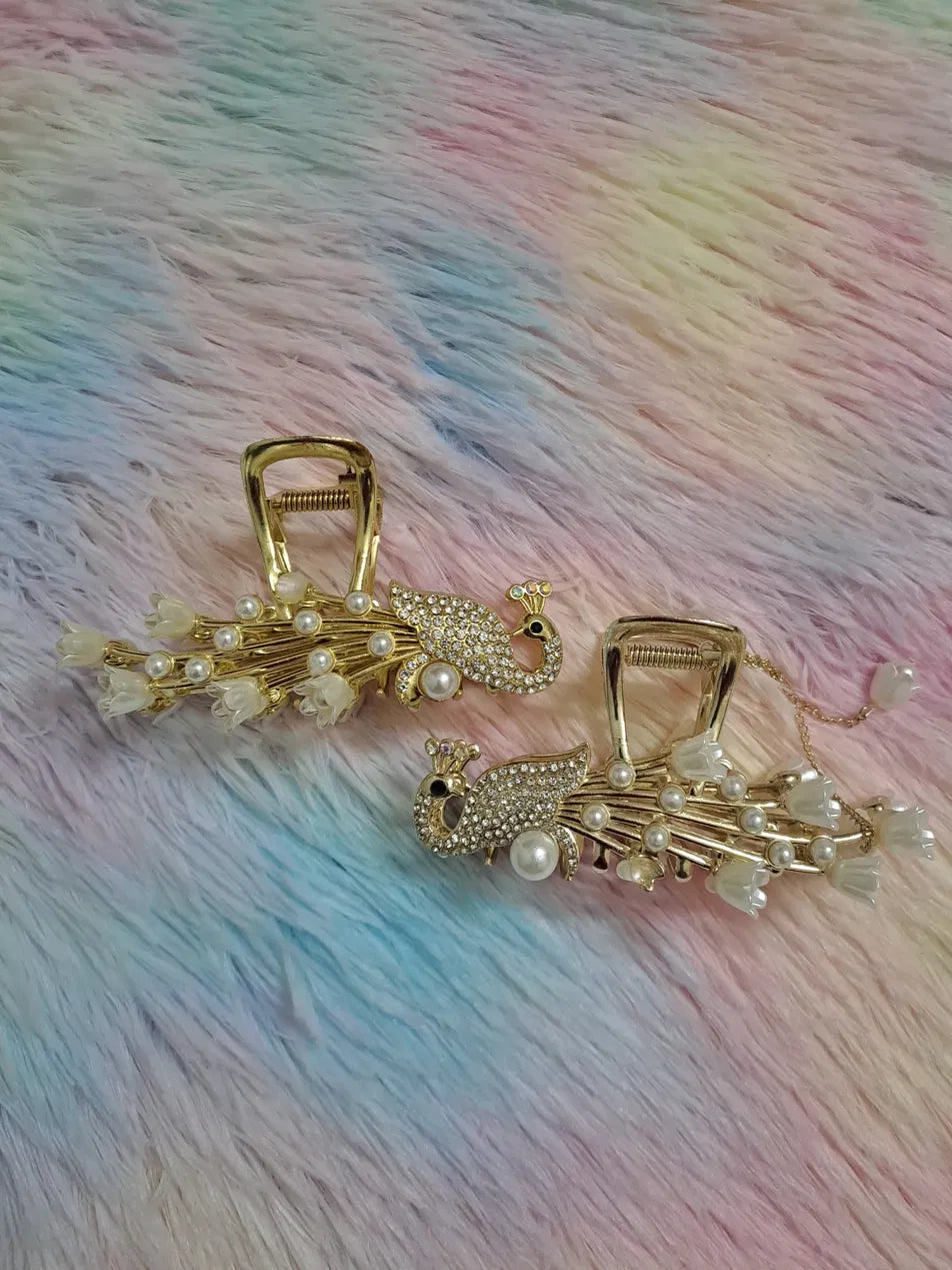 Gold peacock rhinestone pearl hair claw clip set of 2 featuring fully jewelled rhinestone peacock bird figurine with pearl chest accent and black eye, radiating gold metalwork spokes tipped with white flower blossoms and pearl accents, luxury bridal occasion hair accessory