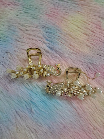 Gold peacock rhinestone pearl hair claw clip set of 2 featuring fully jewelled rhinestone peacock bird figurine with pearl chest accent and black eye, radiating gold metalwork spokes tipped with white flower blossoms and pearl accents, luxury bridal occasion hair accessory